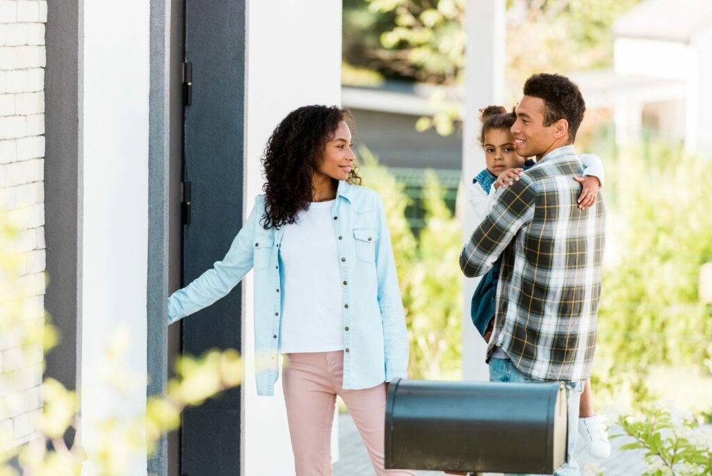 Family arriving at a home, with one adult opening the front door while another carries a child.