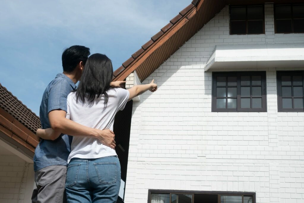 Prospective homeowners standing outside a house and pointing toward the roof during a property tour.
