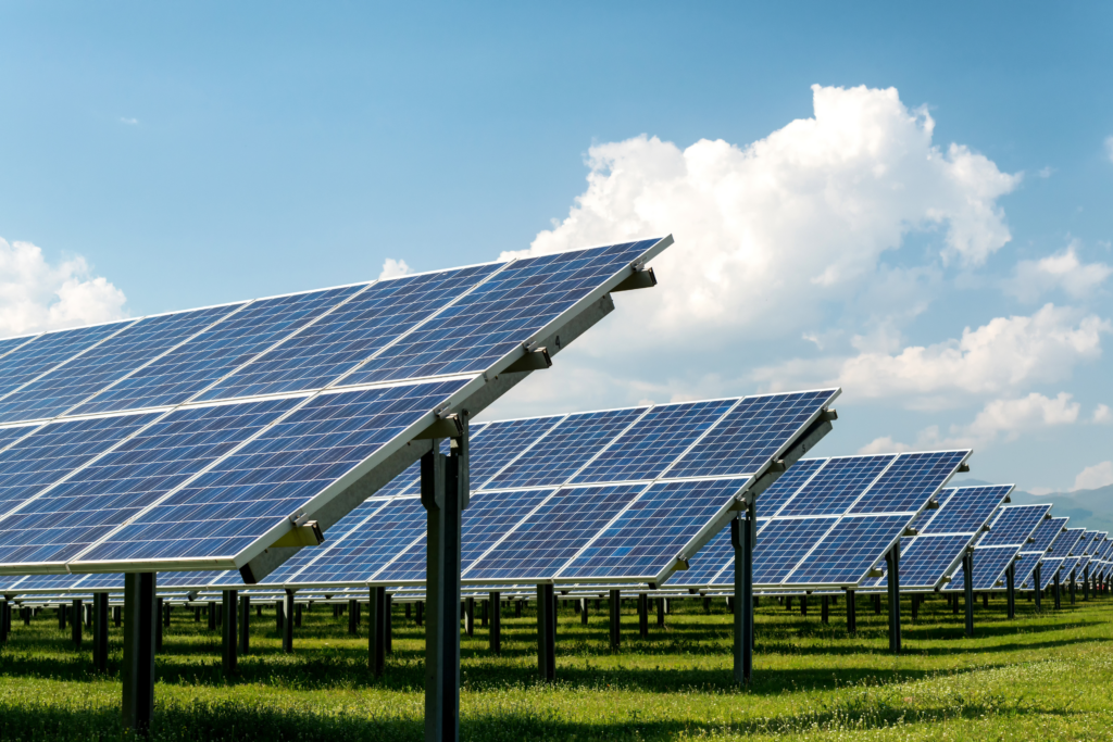 Solar Panel Array in Open Field on a Sunny Day Rows of solar panels mounted on metal supports in a grassy field under a blue sky with scattered clouds, capturing sunlight to generate renewable energy.