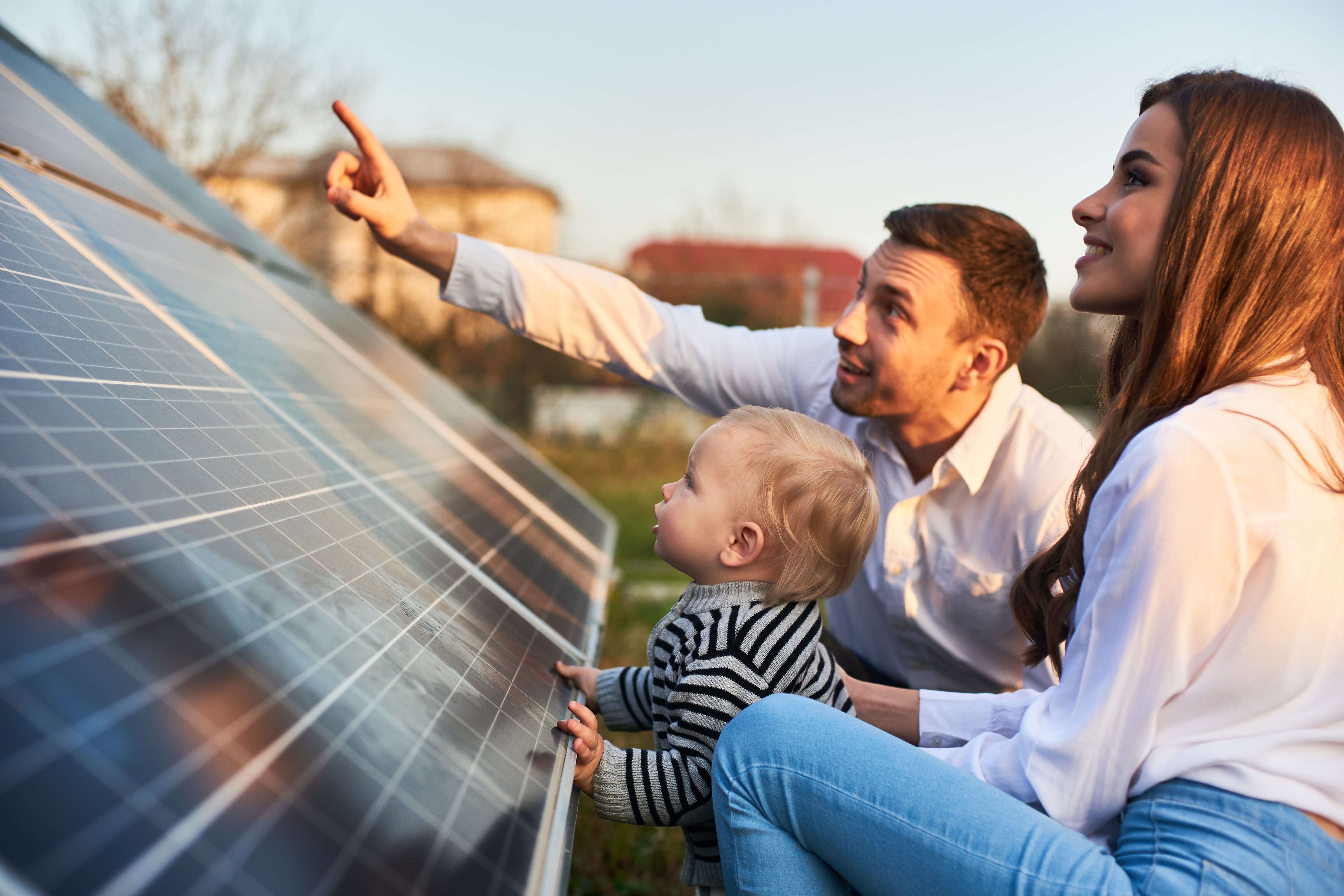A young family with a toddler examining solar panels outdoors, with the father pointing toward something in the distance and the mother smiling.