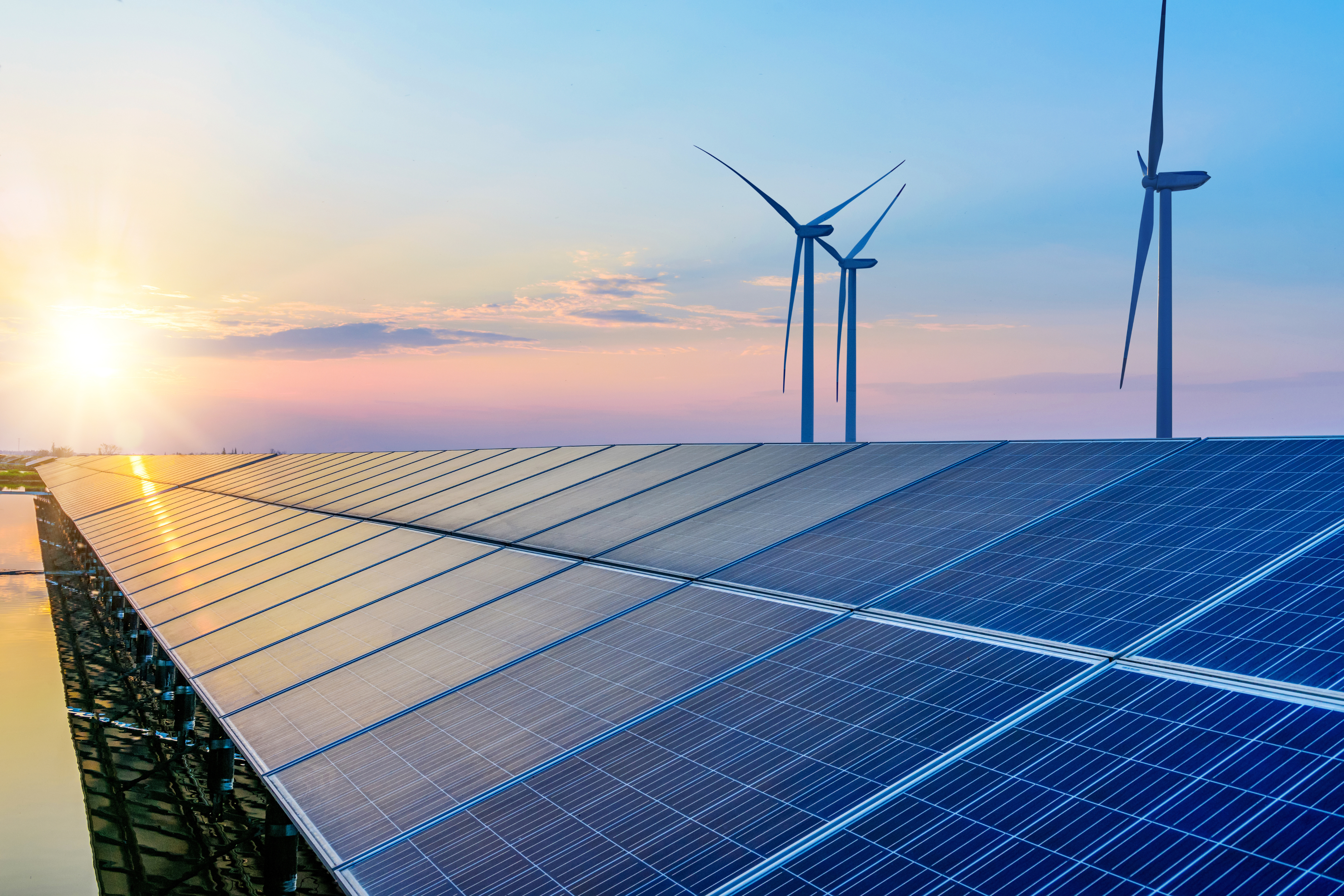 Large solar panel installation with wind turbines in the background at sunset, representing renewable energy sources working together.
