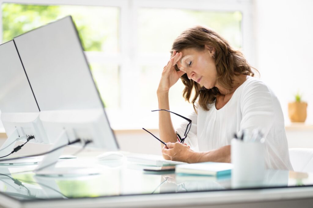 Blog Images (3) Person sitting at a desk holding eyeglasses and looking at paperwork, illustrating financial stress, debt concerns, or budgeting challenges.