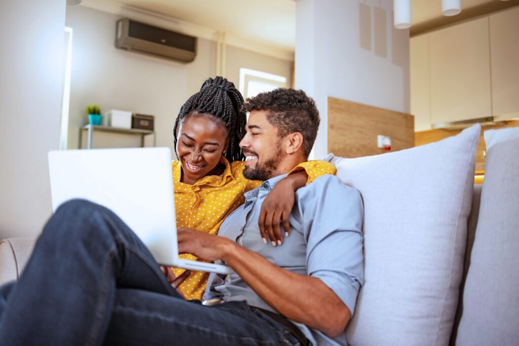 Picture39 People sitting together on a couch using a laptop in a modern home, reviewing information related to homeownership or finances.
