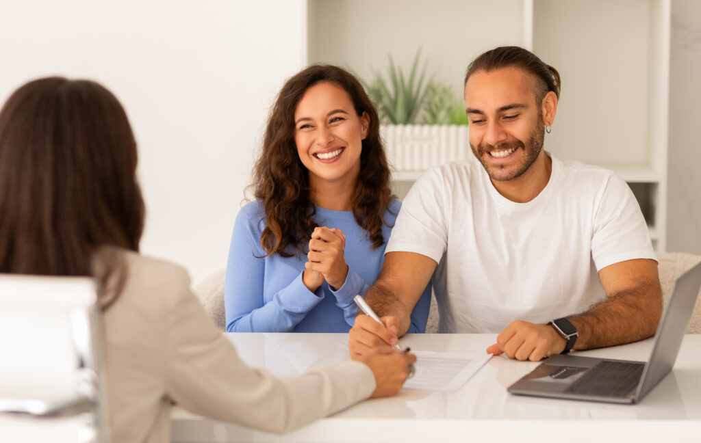 Delighted young couple singing papers at real estate agent office