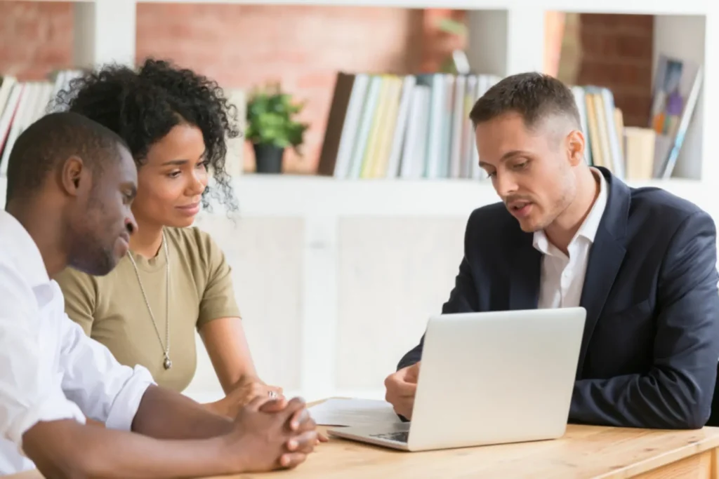 Two clients meeting with a financial professional at a desk, reviewing information on a laptop.
